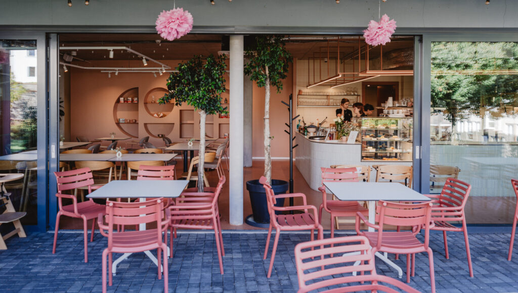 Kaviareň Giselle – otvorená terasa s ružovými stoličkami a výhľadom na bar, vitrínu dezertov a zeleň v útulnom interiéri.