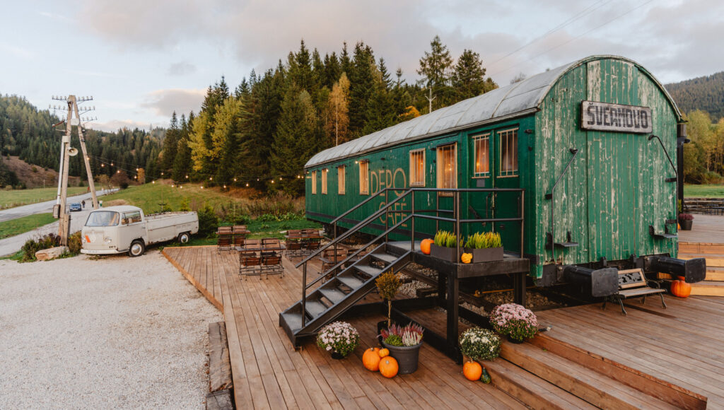 Horská kaviareň Depo Café v Telgárte: zelený historický vagón „Švermov“, drevená terasa s posedením, tekvice, kvety a biely VW Transporter na pozadí tatranského lesa.