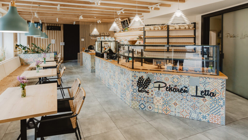 Svetlý interiér Pekárne Letia v Hanušovciach s mozaikovým pultom, vitrínou a pohodlným sedením.