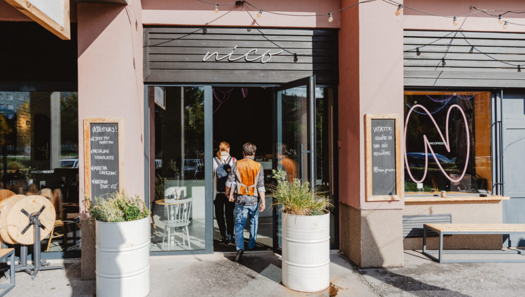 Vstup do kaviarne Nico v Prešove – otvorené dvere, neónové logo a kvetináče pred prevádzkou.