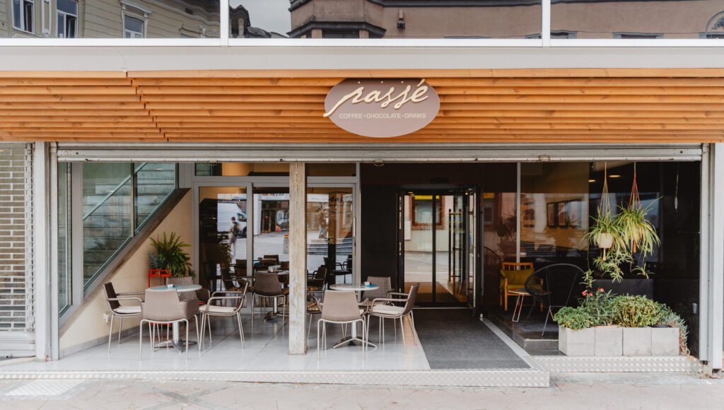 Exteriér kaviarne Passé v Ružomberku – presklený vstup, terasa so stolíkmi a zeleňou, logo „coffee · chocolate · drinks“.