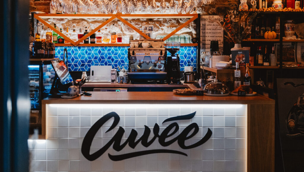Bar Cuvée: dvojpákový kávovar Nuova Simonelli, čierny mlynček, visuté poháre na víno, modrý hexagonálny obklad a back-lit logo Cuvée.