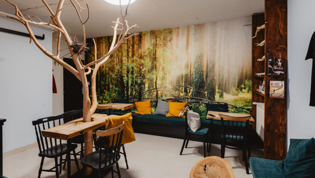 Interiér Street Café: stromový stôl, čierne stoličky, lavica s vankúšmi a veľká lesná tapeta.